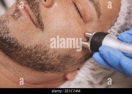 Cropped close up of a mature bearded man relaxing, getting rf-lifting treatment at beauty clinic. Professional cosmetology using rf-lifting machine on Stock Photo