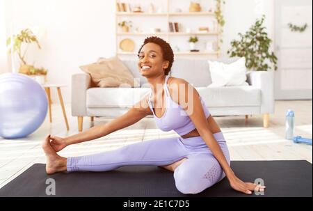 Domestic sports concept. Flexible young African American woman doing exercises on mat at home Stock Photo