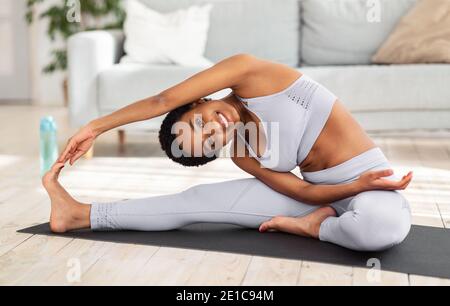 Attractive sporty black woman doing warming up stretching exercses on yoga mat in her home gym Stock Photo