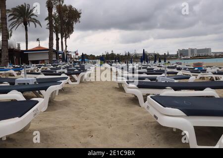 Bad weather. Vaccation near mediterranean Sea in Ayia Napa, Cyprus. Blue and white deck chairs by the sea. Sandy beach in rainy weather. Tourists are Stock Photo