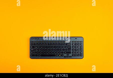 Black computer keyboard on yellow background with copy space. Overhead view. Stock Photo