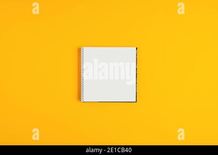 Blank spiral notepad or notebook in square shape on yellow background with copy space. Stock Photo