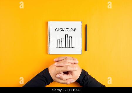 Hands of a businessman and a notebook with the word cash flow and a chart written on it. Corporate cash flow analysis concept. Stock Photo