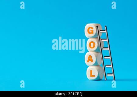 The word goal on tiered wooden cubes with a ladder on blue background. Accomplish or reach goals concept. Stock Photo