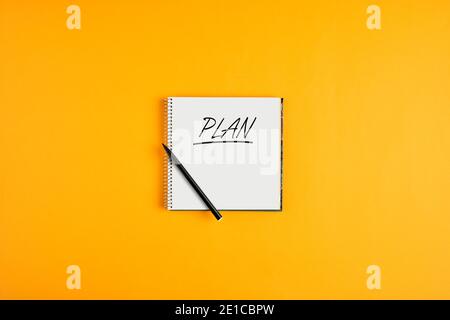 The word plan written on notebook with pen on yellow background. Business plan concept. Stock Photo