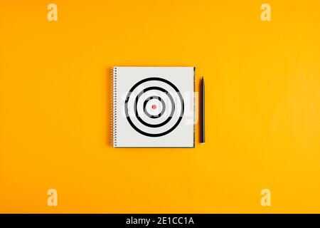 Target icon drawn on a notepad with black pen next to it against yellow background with copy space. Stock Photo
