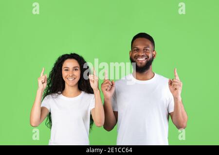 Diverse Couple Pointing Fingers Up Standing Over Green Background Stock Photo