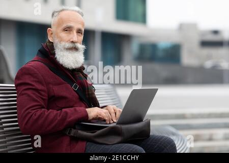 Modern grandfather using laptop while sitting on bench Stock Photo