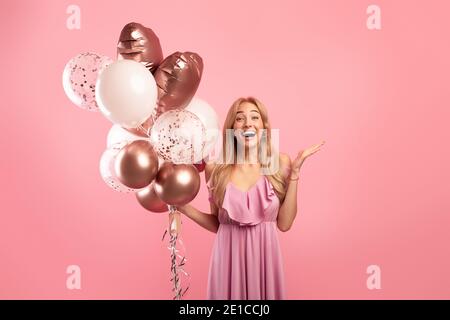 Portrait of excited young lady with bunch of balloons for birthday or Woman's Day, celerating holiday on pink background Stock Photo
