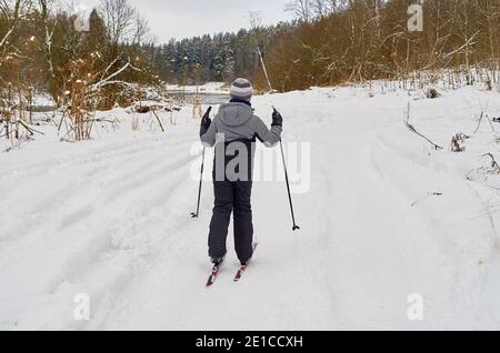 A boy skis on a winter road along the river. View from behind. Stock Photo