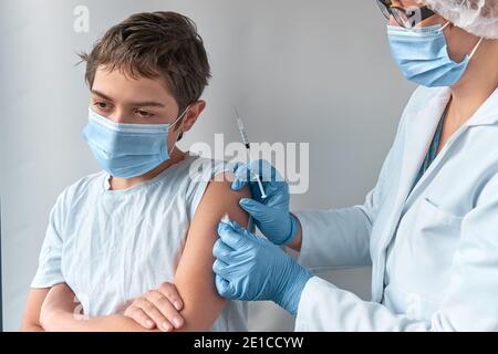 Close-up on hands in gloves with syringe and shoulder of the patient, teen kid. Covid 19, flu, tetanus or measles vaccine concept. Medic, doctor or Stock Photo