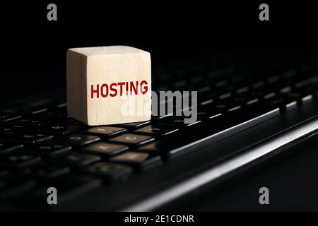 The word hosting on wooden block with computer keyboard against black background. Computer or web hosting concept. Stock Photo