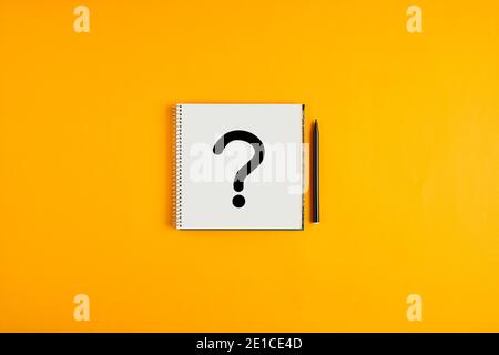 Question mark drawn on a notepad with black pen next to it against yellow background with copy space. Stock Photo