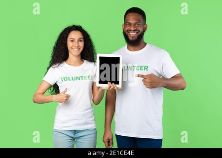 Volunteers Holding Tablet Pointing At Computer Screen On Green Background Stock Photo