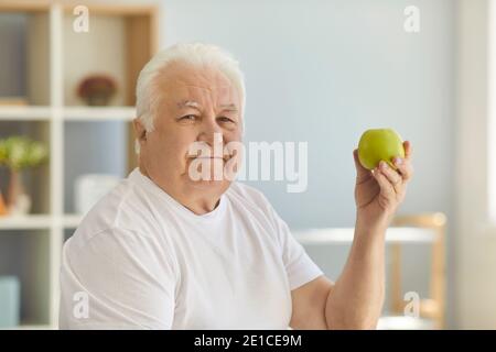 Senior man holding green apple and recommending eating raw fruit and keeping healthy diet Stock Photo