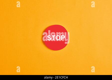 Red round button with the word stop against yellow background. Stock Photo