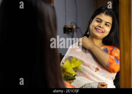 a beautiful Indian woman adjusting her white saree in front of mirror with smiling face Stock Photo