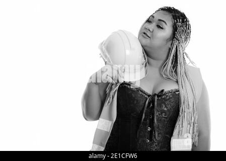 Young fat Asian construction woman holding safety helmet near the face while thinking Stock Photo