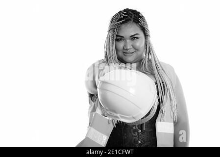 Young happy fat Asian construction woman smiling while pointing safety helmet at camera Stock Photo