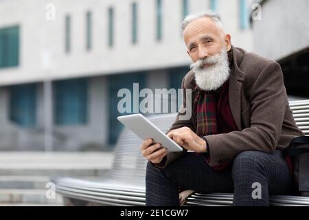 Modern aged man sitting on bench and using digital tablet Stock Photo