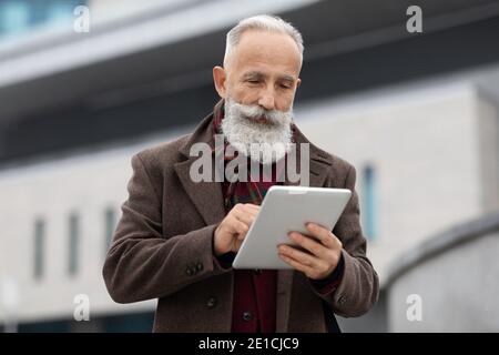 Wealthy senior man using digital tablet outdoors Stock Photo