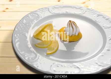 Lemon cream tart with meringue brule and lemon slices on white plate on wooden table Stock Photo