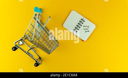 Overshot of small shopping cart and notebook with Happy New Year text on it  Stock Photo