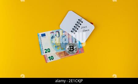 Overheadshot of Revolut credit card, euro banknotes,bitcoin and a small notebook with '2021 goals' text on it Stock Photo