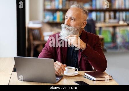 Thoughtful senior man sitting at cafe, using laptop Stock Photo