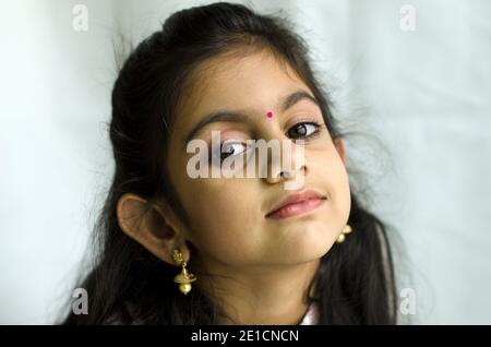 PORTRAIT OF A LITTLE INDIAN GIRL IN A GENTLE SMILE WITH BINDI AND TRADITIONAL INDIAN EAR RING. Stock Photo