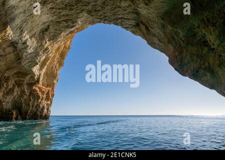 A view from inside a cave on the ocean coast with turquoise water and sunny blue sky outside