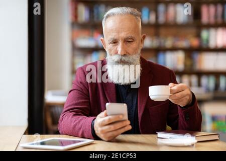 Grey-haired elderly man drinking coffee and using phone Stock Photo
