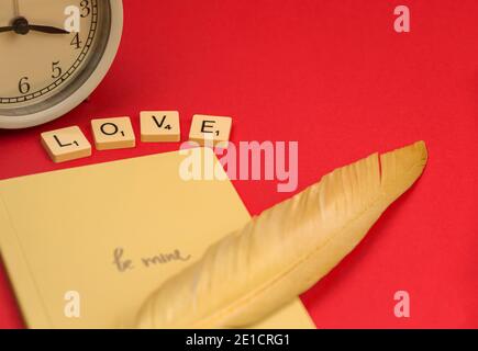 Love letter, envelop notebook with yellow feather, word love with cubes, Valentine's Day concept, red background Stock Photo