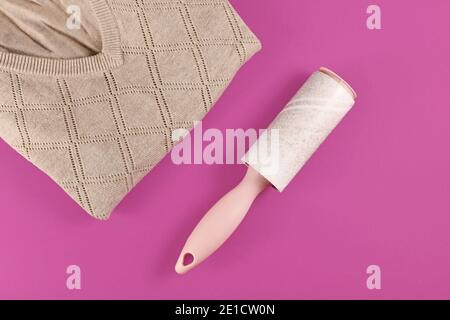 Used fluff roller next to folded sweater on dark pink background Stock Photo