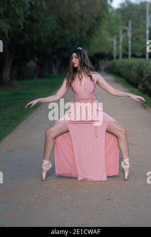 Young teenage woman wearing pink dress standing on pointe dancing ballet outdoors Stock Photo