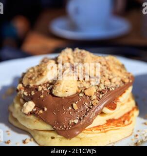 Pancakes with chocolate sauce on a white plate. Traditional American breakfast. Heap of fresh baked hot pastry with cocoa cream, fruits, walnuts. Blur Stock Photo