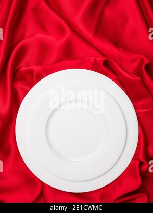 Valentines dinner concept. Vertical top view of empty set white plates on red satin background. Formal blank dishware on silk cloth passion red color Stock Photo