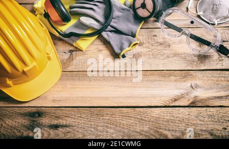 Construction work safety concept. Protective yellow hard helmet, headphones, gloves, work vest, mask and goggles on wooden background. Protection and Stock Photo