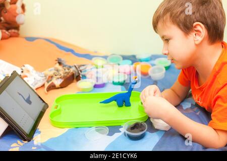 Cute 7 years old boy sculpts brachiosaurus from plasticine on his bed in kid room Stock Photo