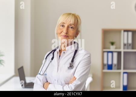 Smiling elderly woman doctor thetapist in white medical uniform standing and looking at camera Stock Photo
