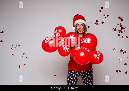 Cheerful girl with balloons and flying heart-shaped confetti and discount sign looking at camera under falling heart-shaped confetti.. Stock Photo