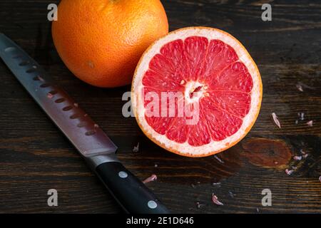 Red Grapefruit Sliced in Half: A whole and halved pink grapefruit on a dark wood cutting board Stock Photo