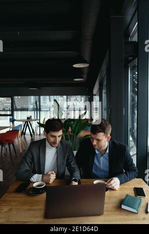 Two businessmen talking about new opportunities sitting with laptop at desk, planning project, considering business offer, sharing ideas Stock Photo