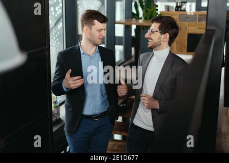 Two men walking down on wooden stairs chatting indoors. Communication concept Stock Photo