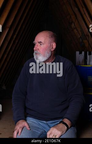 Bearded old man sitting in his attic. Stock Photo