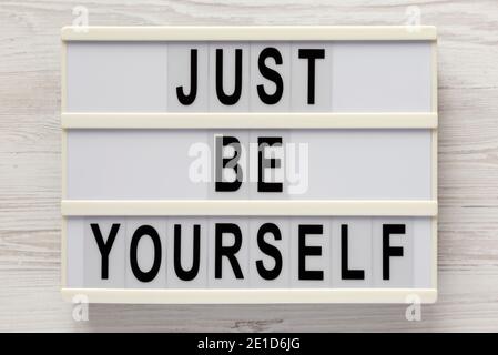 'Just be yourself' on a lightbox on a white wooden surface, top view. Flat lay, overhead, from above. Stock Photo
