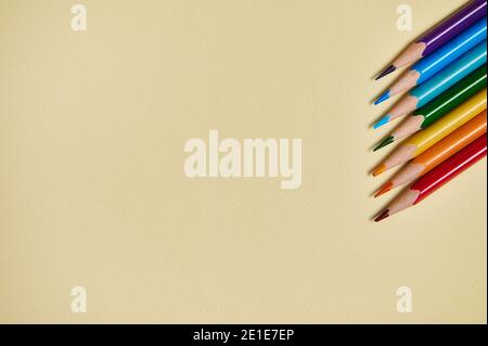 Colored pencils form the colors of rainbow on a yellow background. Flat lay, copy space, top view. Office Stock Photo