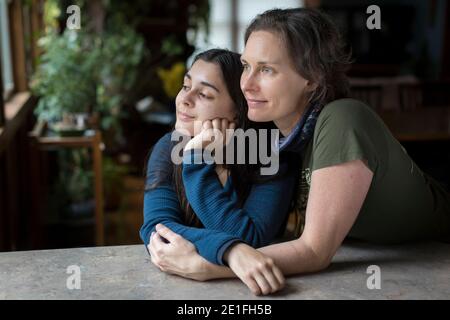 Mother with arms around pretty teen daughter looking off camera Stock Photo
