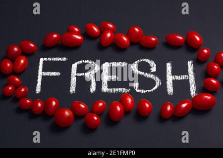 fun shot of the word fresh written with chalk surrounded by healthy fresh vibrant red cherry tomatoes on a blackboard, concept eating fresh healthy lo Stock Photo