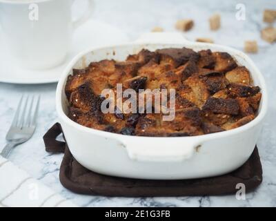 Bread pudding in white baking dish on brown heat pad with table set Stock Photo